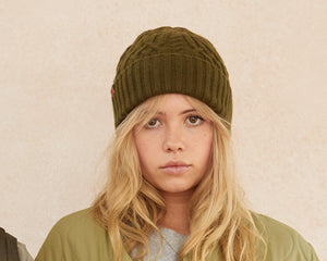 Person wearing a green knit beanie against a beige background