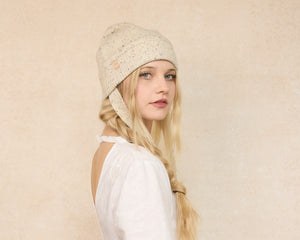 Woman wearing a beige knitted hat with a plain background