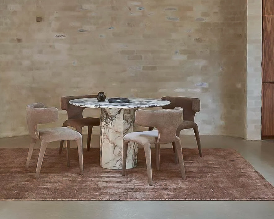 Round marble dining table with ocean toned veining, surrounded by modern cushioned chairs in a well-lit room.