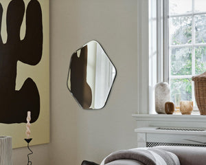 Hexagonal mirror on a wall with abstract art and decor items in the background