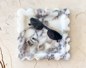 Marble-patterned jewelry dish with sunglasses and rings on a beige marble surface