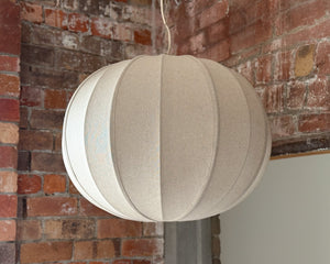Beige spherical lampshade hanging against a brick wall.
