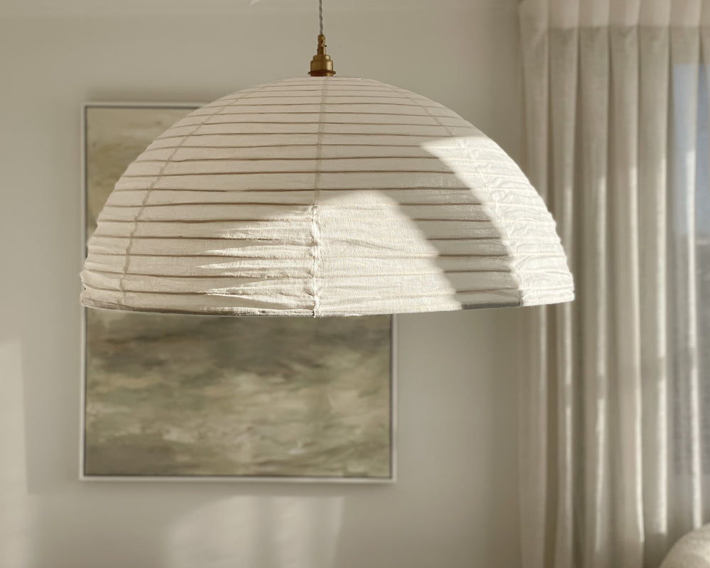 half circle linen light shade in an off white linen colour hung in a bedroom cast in dappled light 