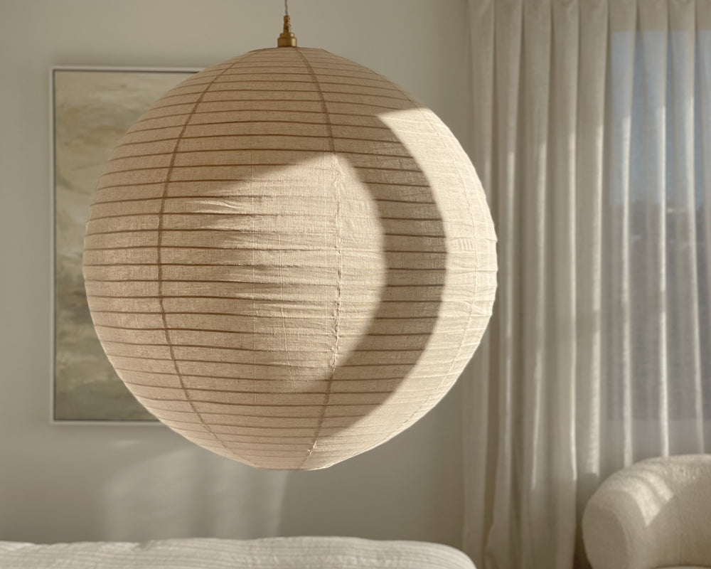 round linen light shade in a natural linen colour hung in a bedroom cast in dappled light 